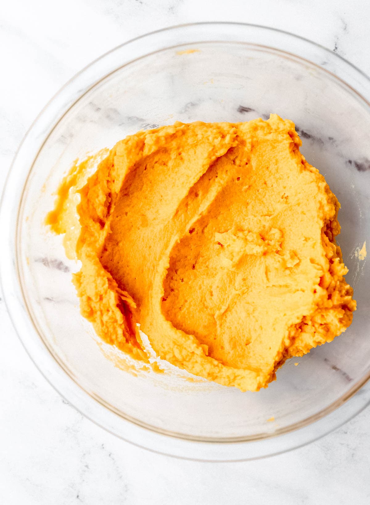Sweet potato and butter combined in glass mixing bowl on marble surface. 