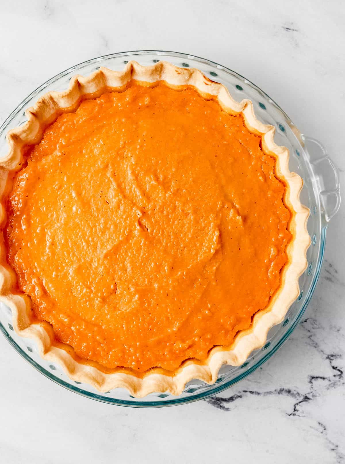 Whole baked pie in glass pie plate on marble surface. 