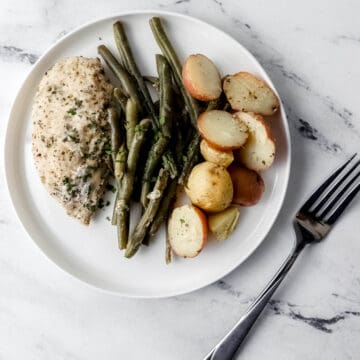 Overhead view of white plate with chicken, potatoes, and beans on it beside a fork.