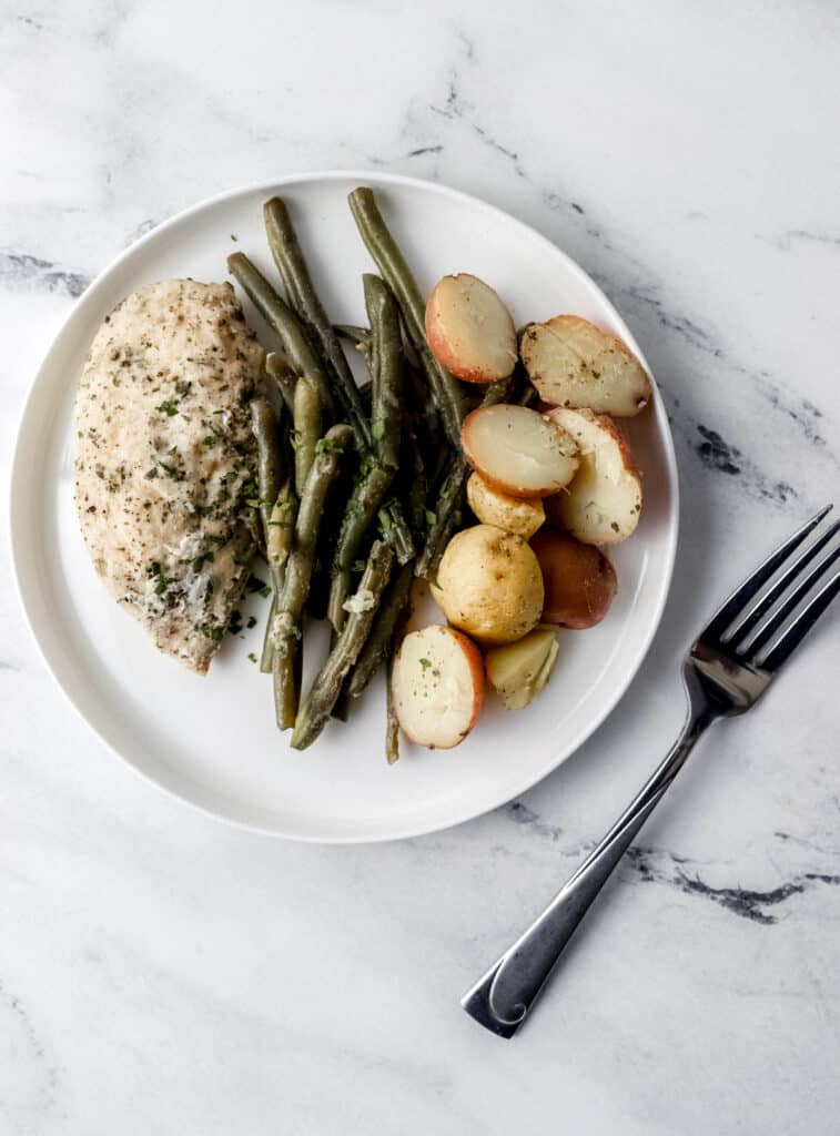 Overhead view of white plate with chicken, potatoes, and beans on it beside a fork.