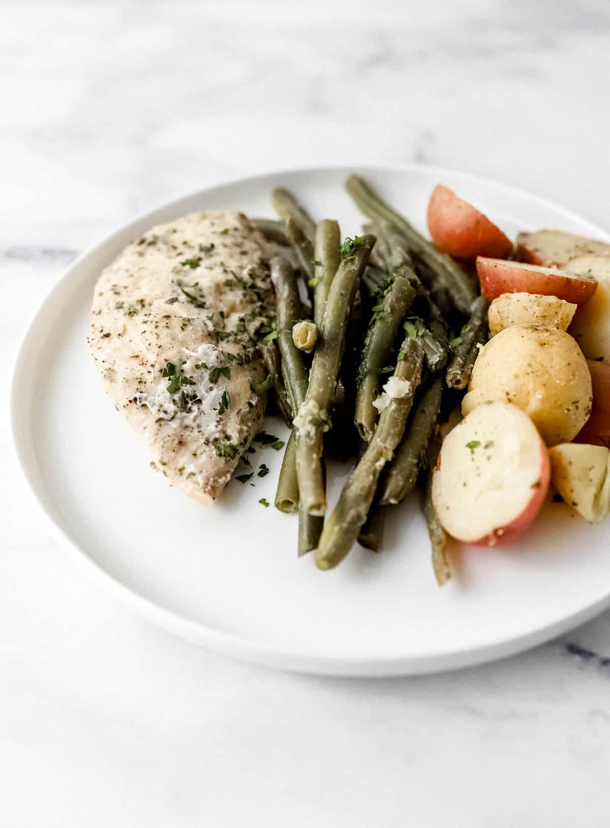 Close up side view of serving of chicken and vegetables on white plate. 