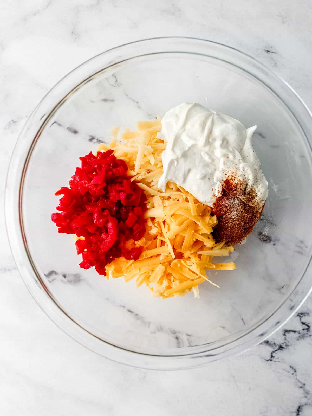 Ingredients to make pimento cheese added to large glass mixing bowl. 