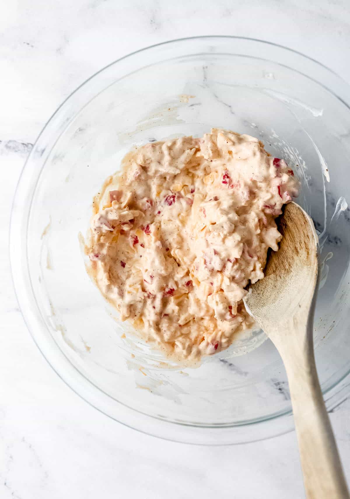 Pimento cheese in glass mixing bowl with wooden spoon. 