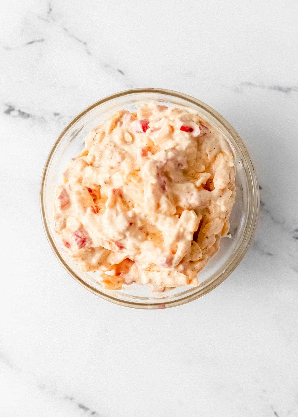 Overhead view of pimento cheese in small glass bowl on marble surface. 