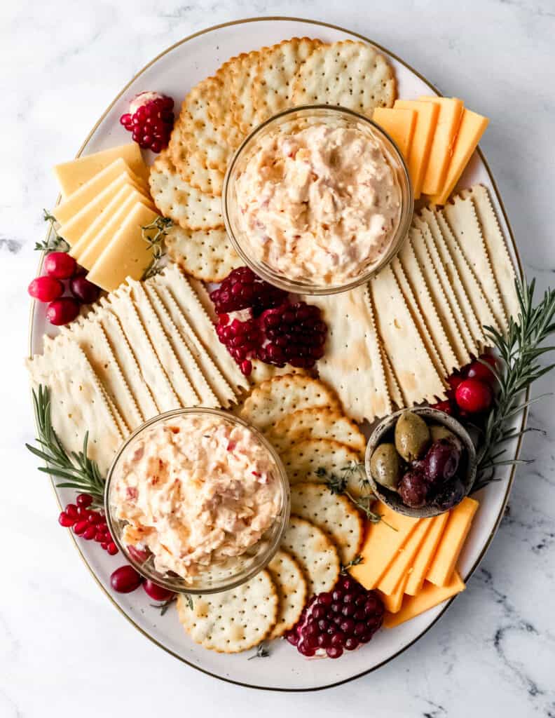 Overhead view of snack board with two small glass bowls of pimento cheese.