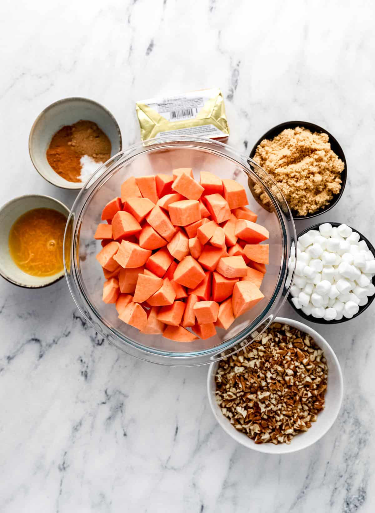 Ingredients needed to make sweet potato casserole in separate bowls on marble surface. 