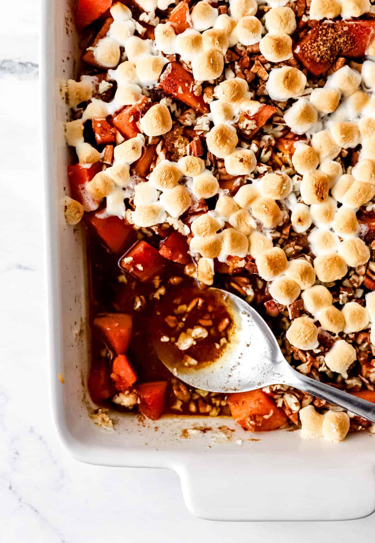 Overhead baked sweet potato casserole in white baking dish with a large serving spoon. 