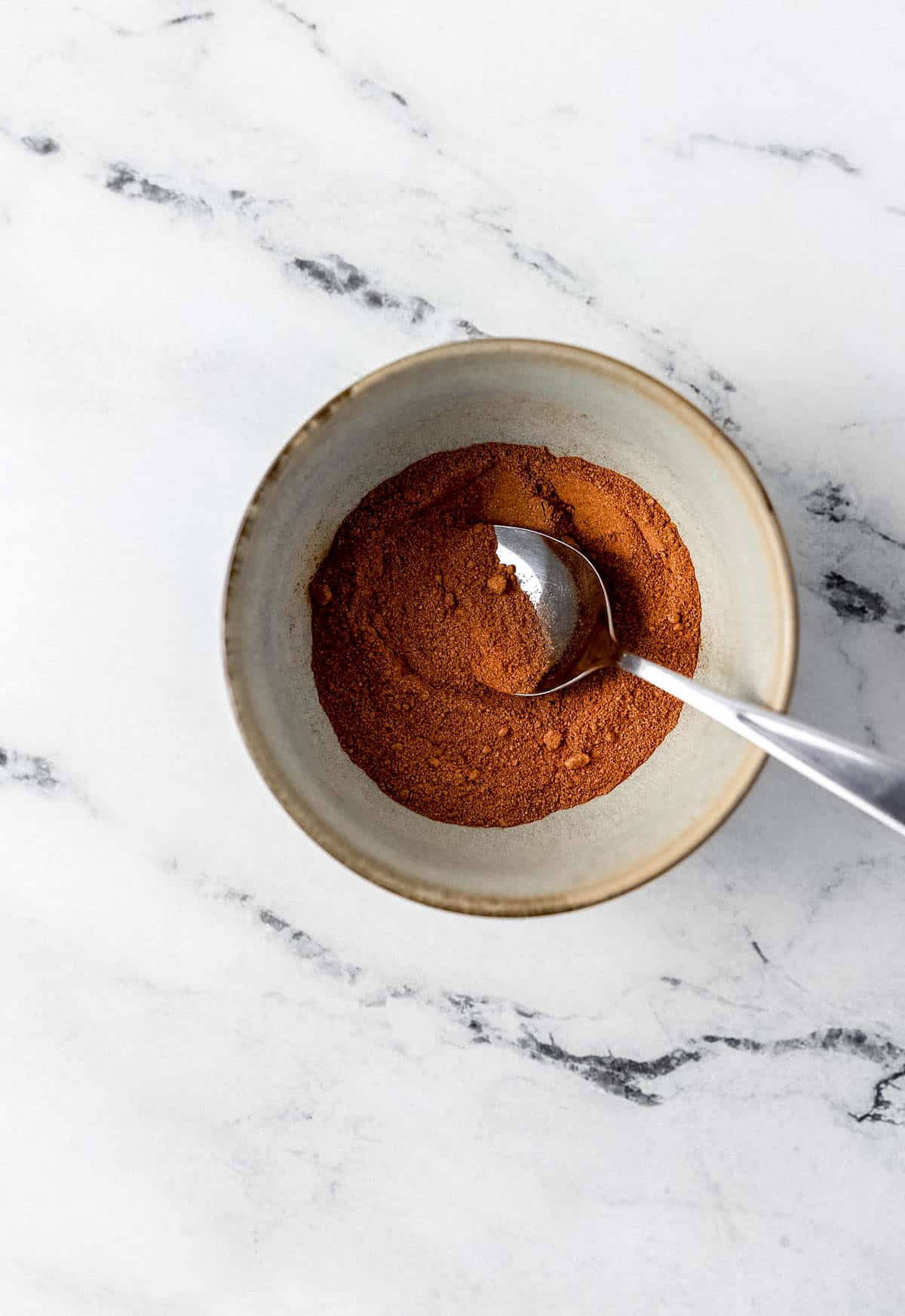 Brown sugar, cinnamon, nutmeg, in small bowl with spoon. 