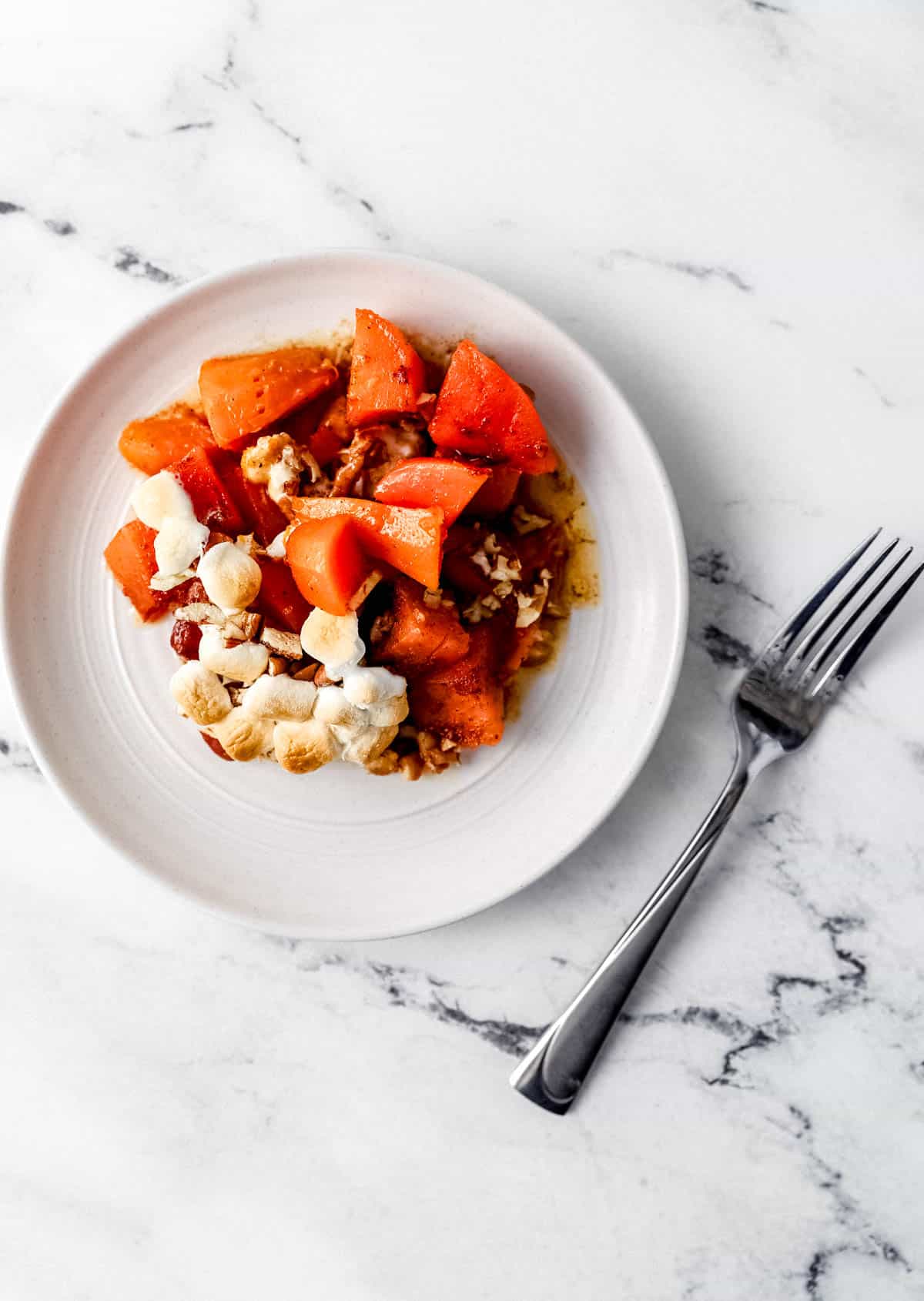 Overhead single serving of sweet potato casserole on white plate beside a fork. 