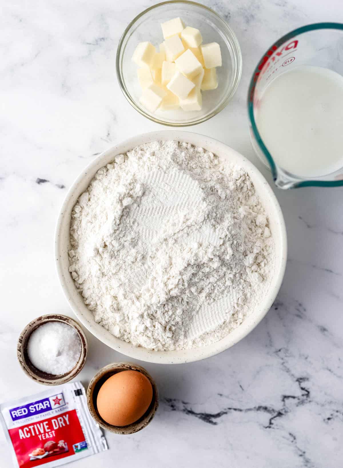 Overhead view of ingredients needed to make rolls in separate bowls on marble surface. 