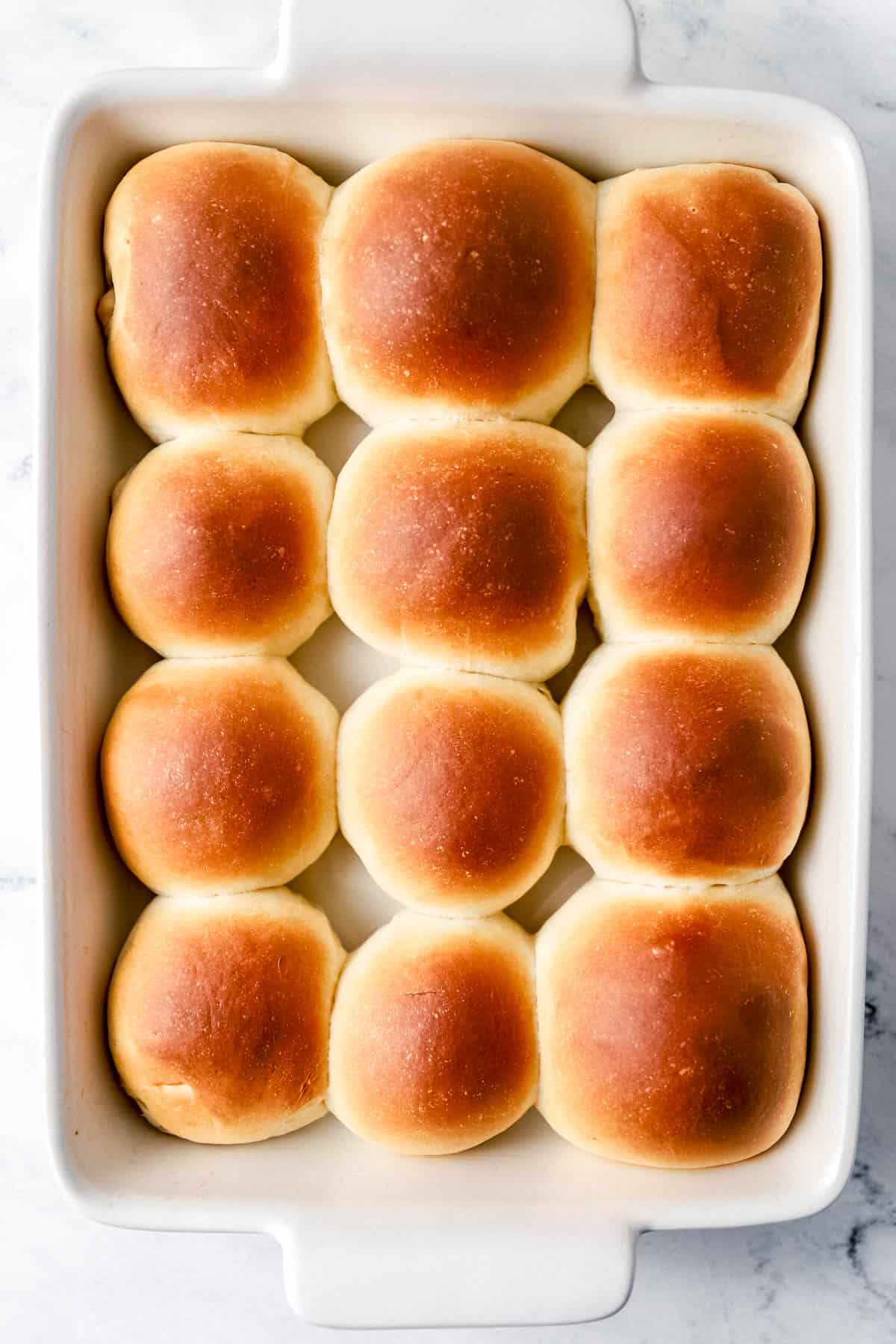 Overhead view of baked rolls in rectangle baking dish on marble surface. 
