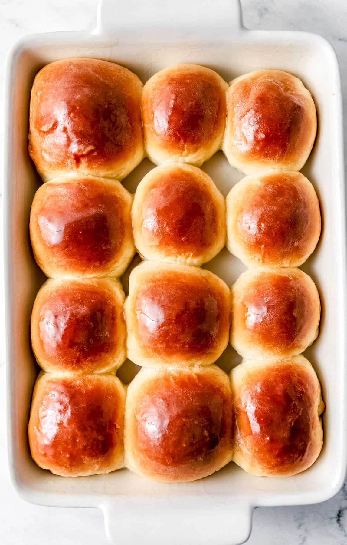 Baked rolls in rectangle baking dish topped with melted butter. 