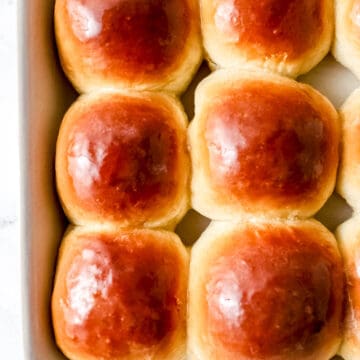 Close up view of baked rolls in white baking dish topped with melted butter.