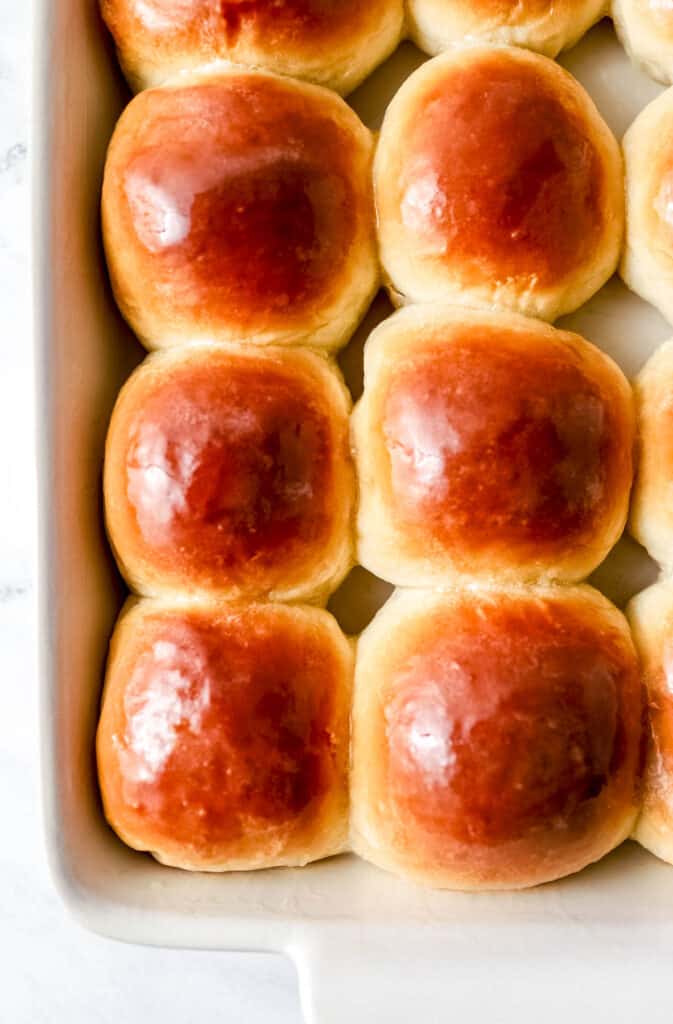 Close up view of baked rolls in white baking dish topped with melted butter.