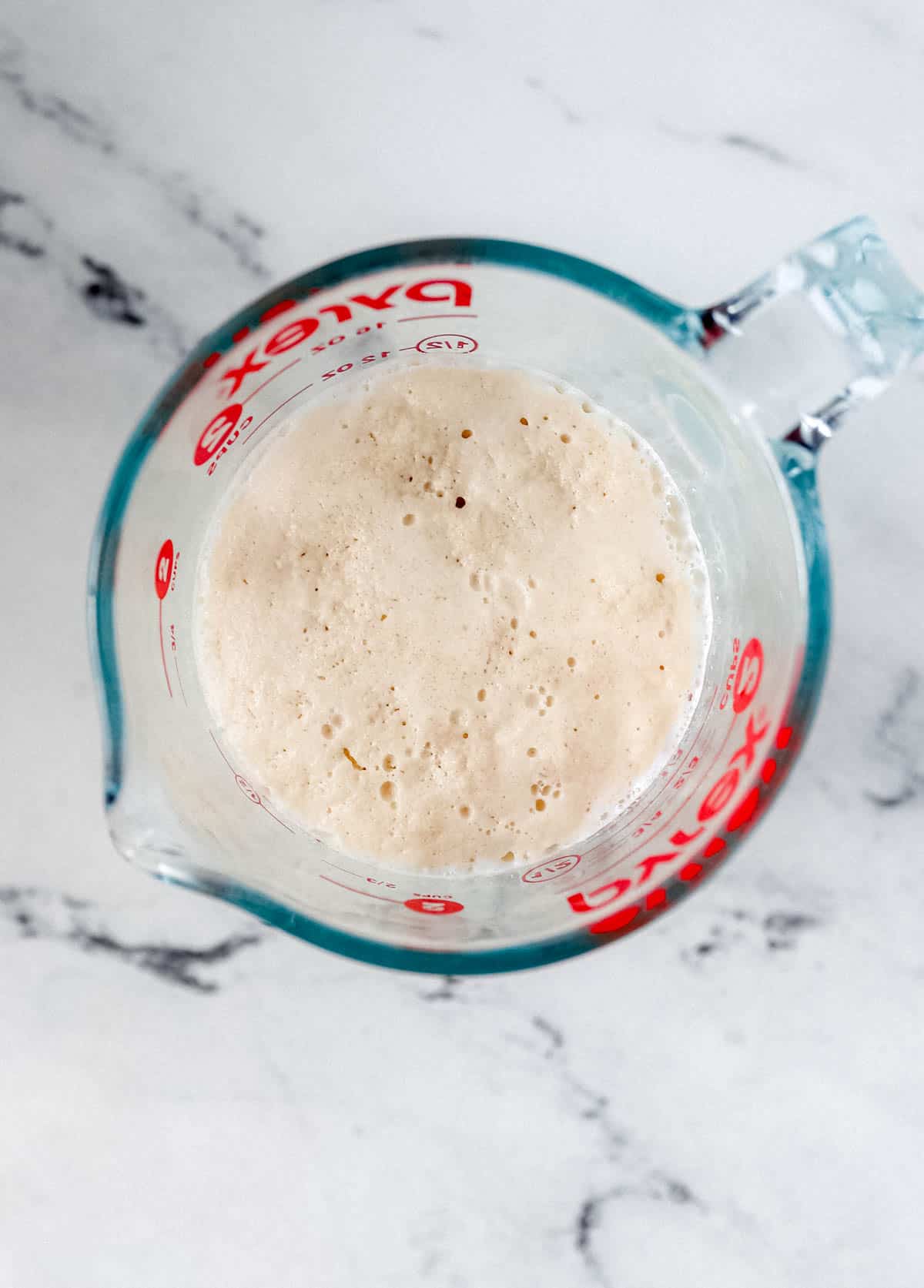 Yeast, sugar, and warm milk in glass measuring cup. 