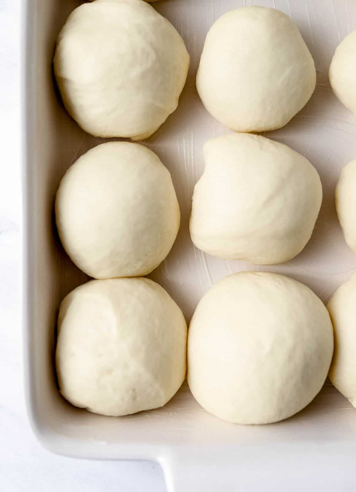 Close up view of dough balls that have risen in white baking dish. 