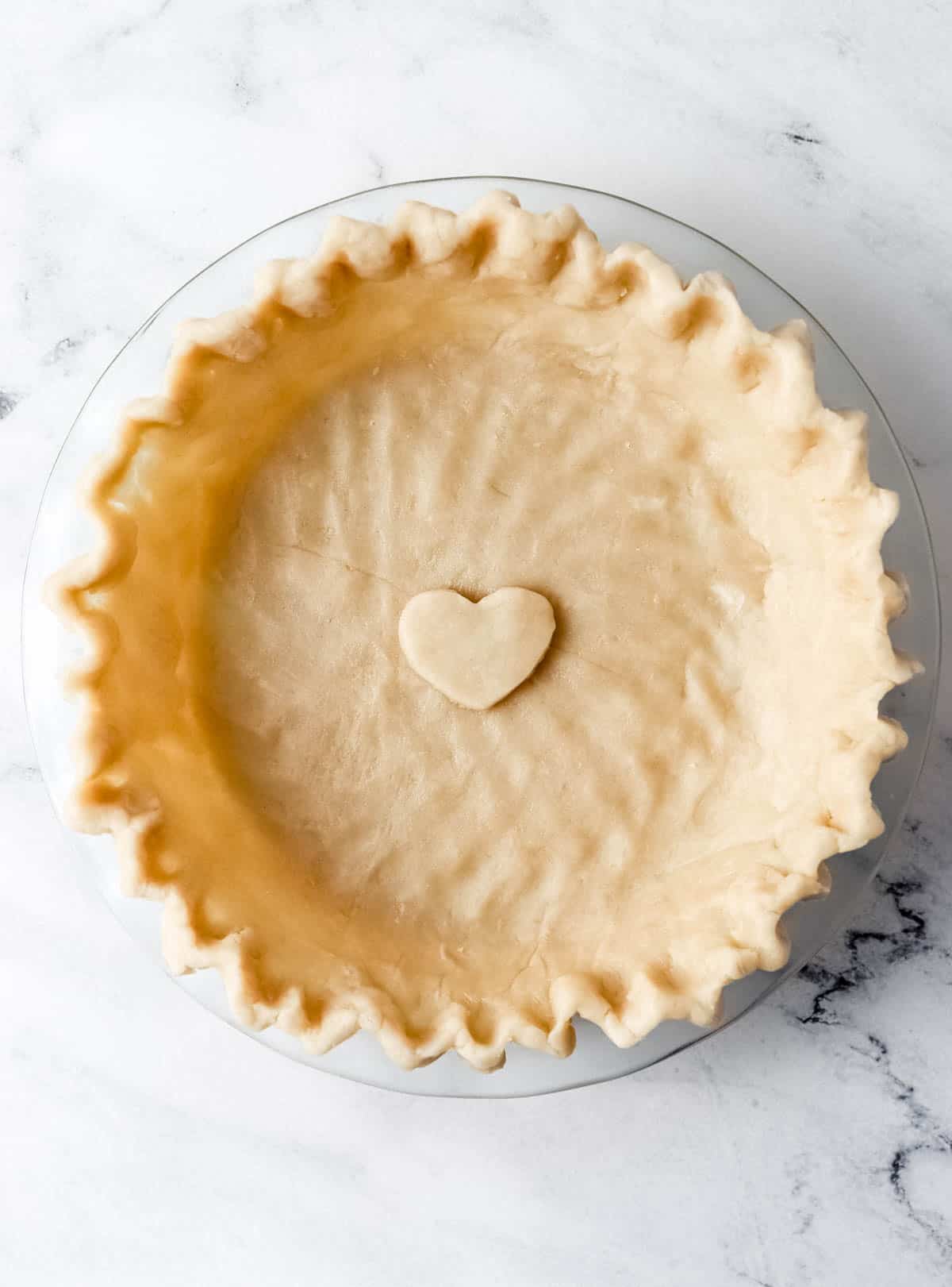 Overhead view of pie crust in glass pie dish on marble surface. 