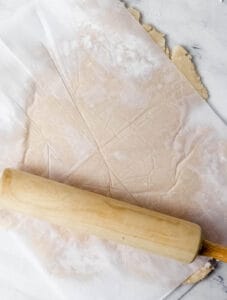 Pie crust rolled out between parchment paper with rolling pin.