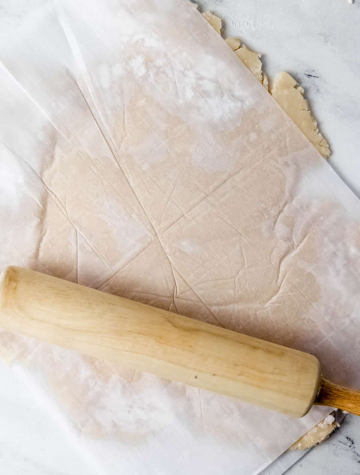 Pie dough rolled out in between two pieces of parchment paper with rolling pin. 