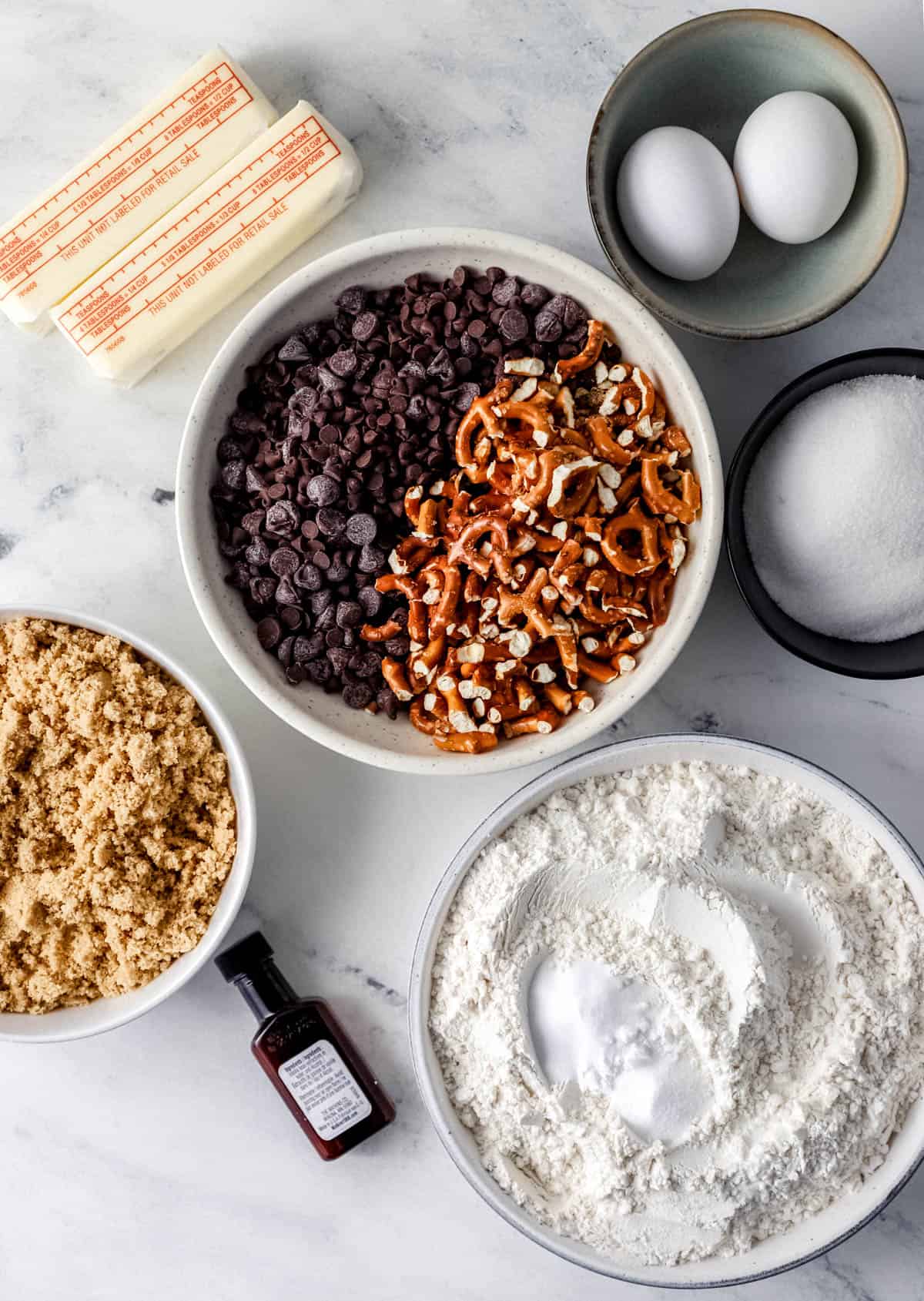 Overhead view of ingredients needed to make cookies in separate bowls on marble surface. 