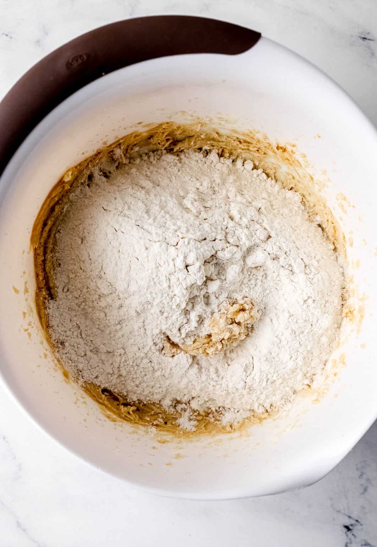 Wet and dry cookie ingredients combined in large white mixing bowl. 