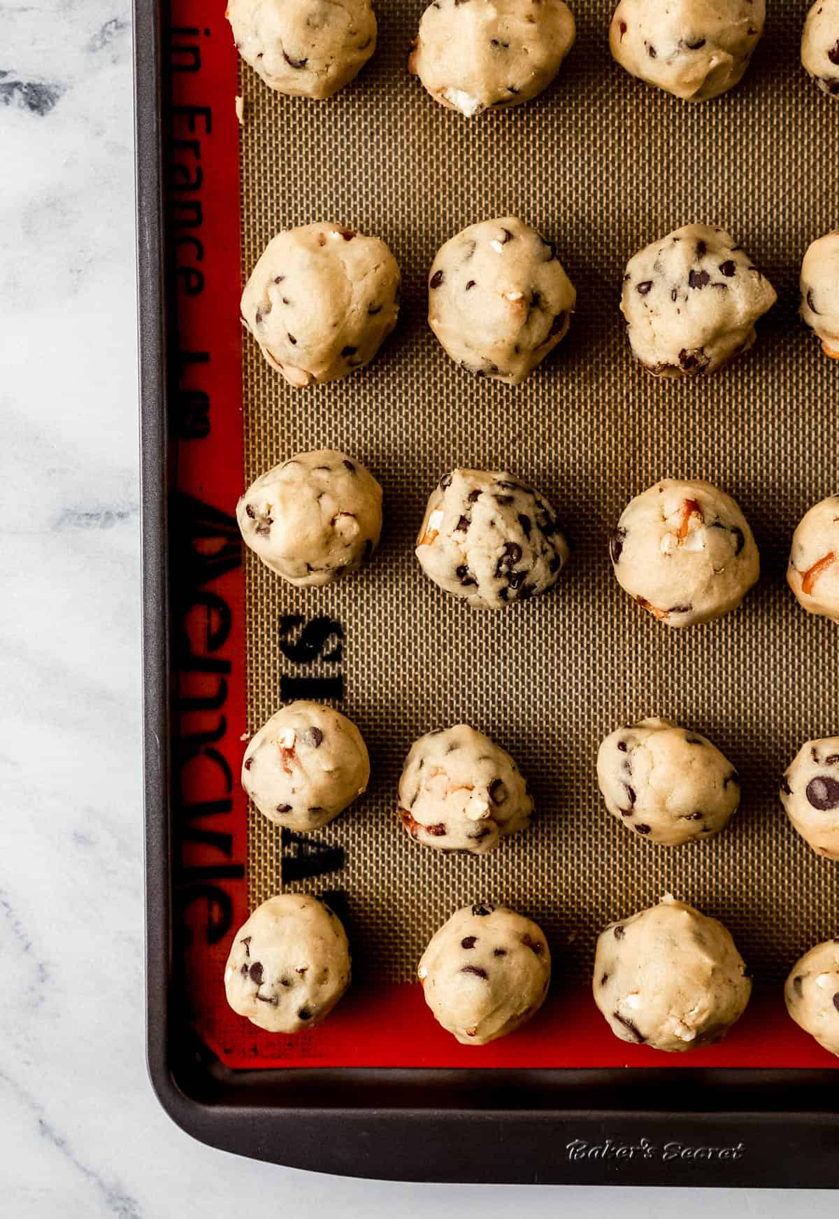 Cookie dough balls added to baking sheet with non stick liner on it. 