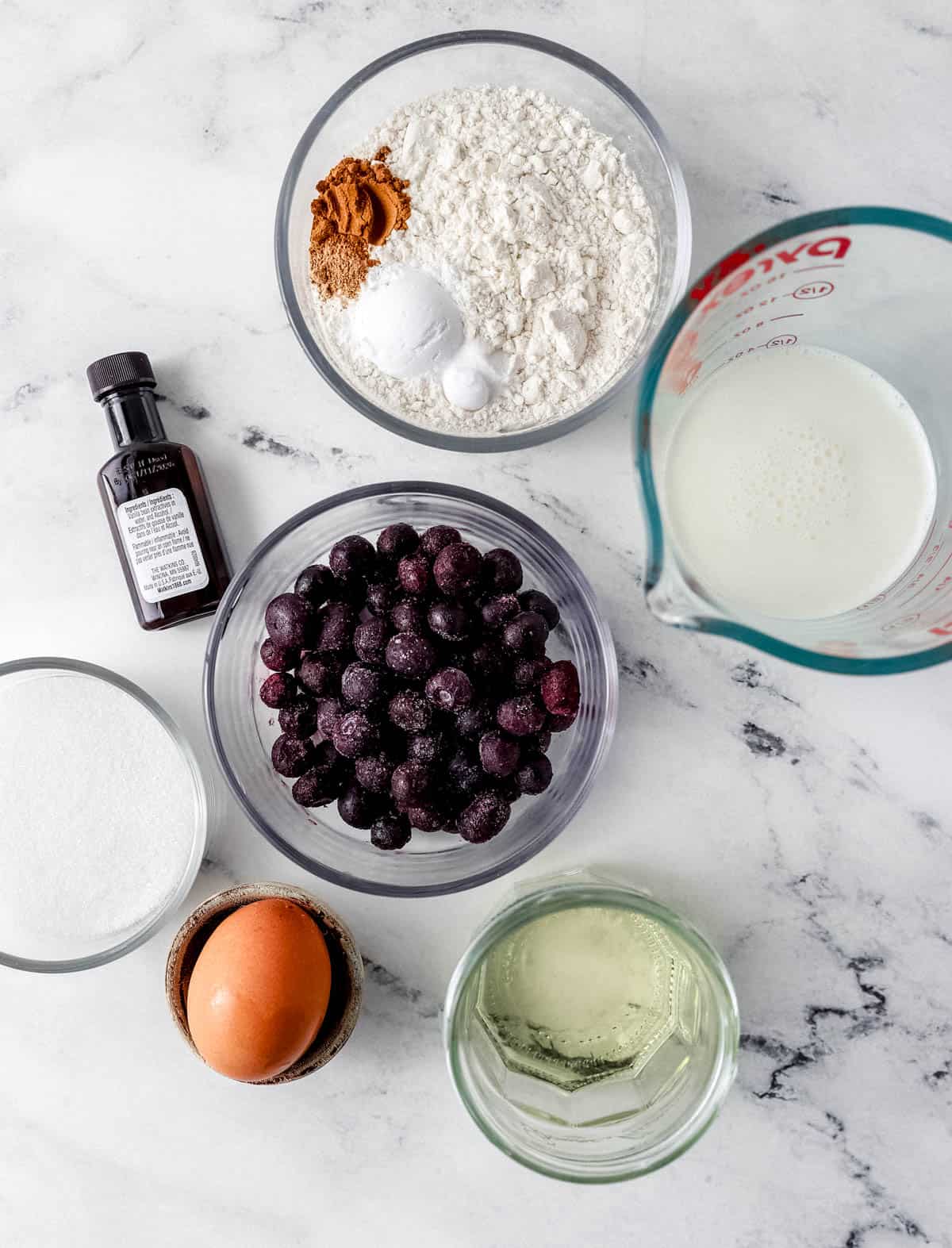 Overhead view of ingredients needed to make muffins in separate bowls on marble surface. 
