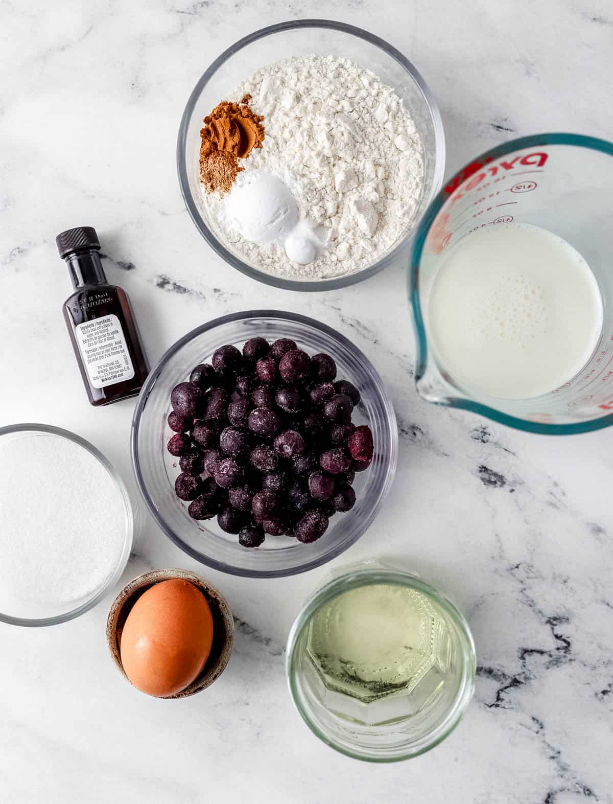 Overhead view of ingredients needed to make muffins in separate bowls on marble surface.