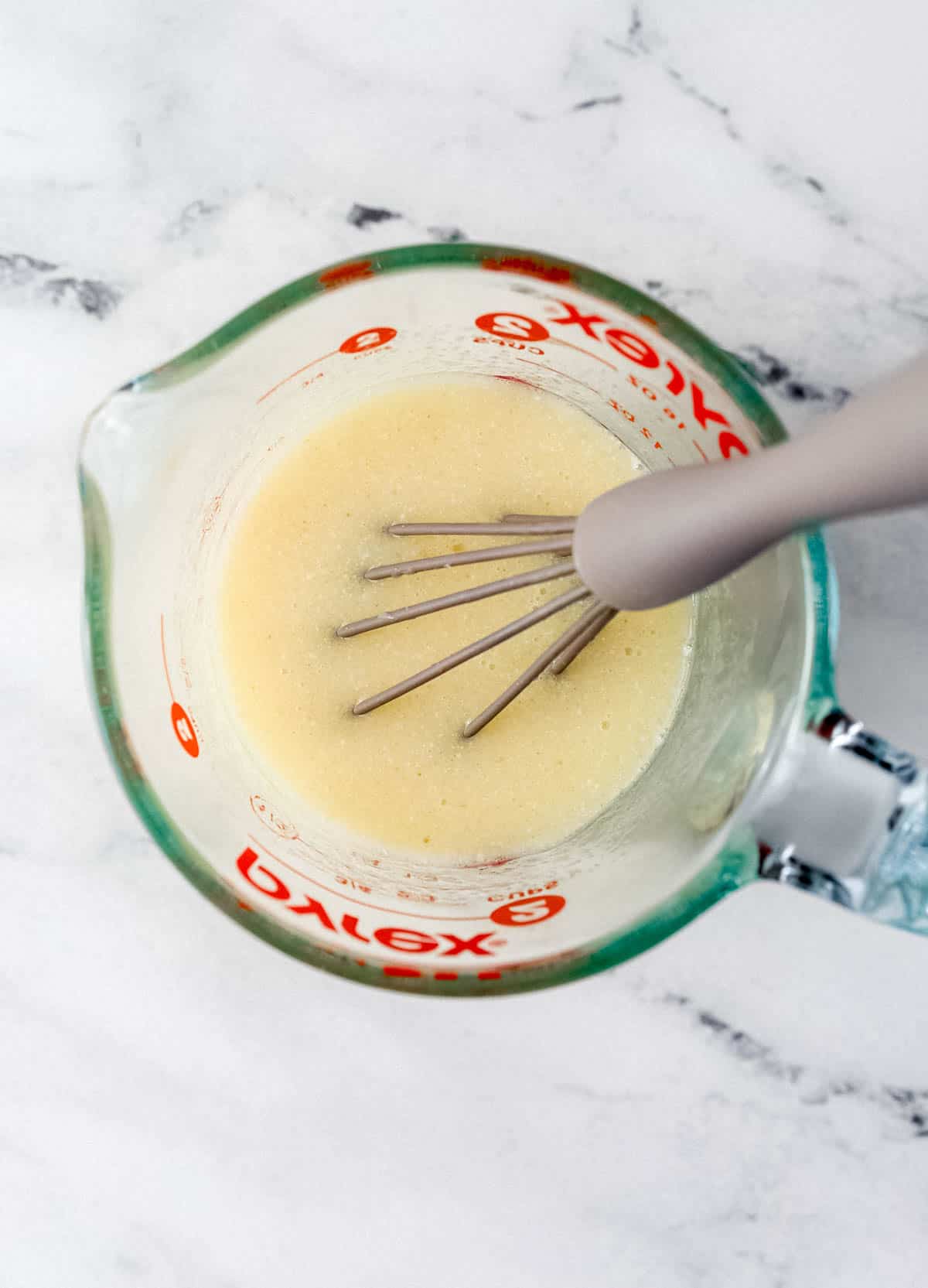 Wet ingredients needed to make muffins in glass measuring cup with whisk.