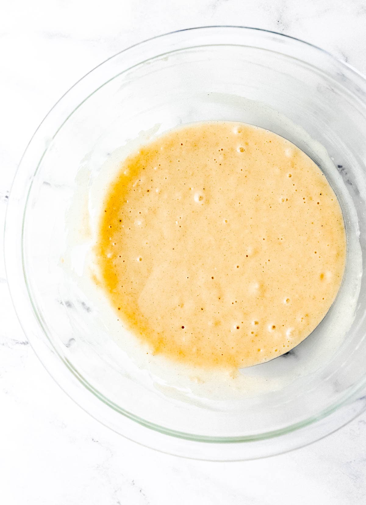 Overhead view of wet and dry ingredients combined in glass mixing bowl. 