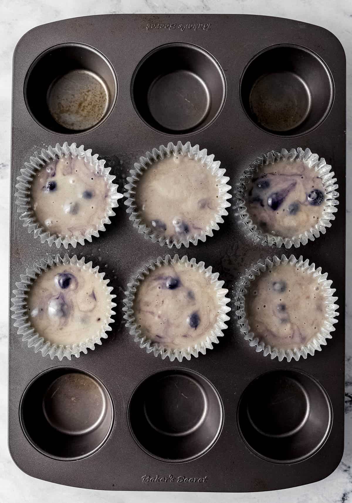 Muffin batter added to baking cups in muffin pan before baking. 