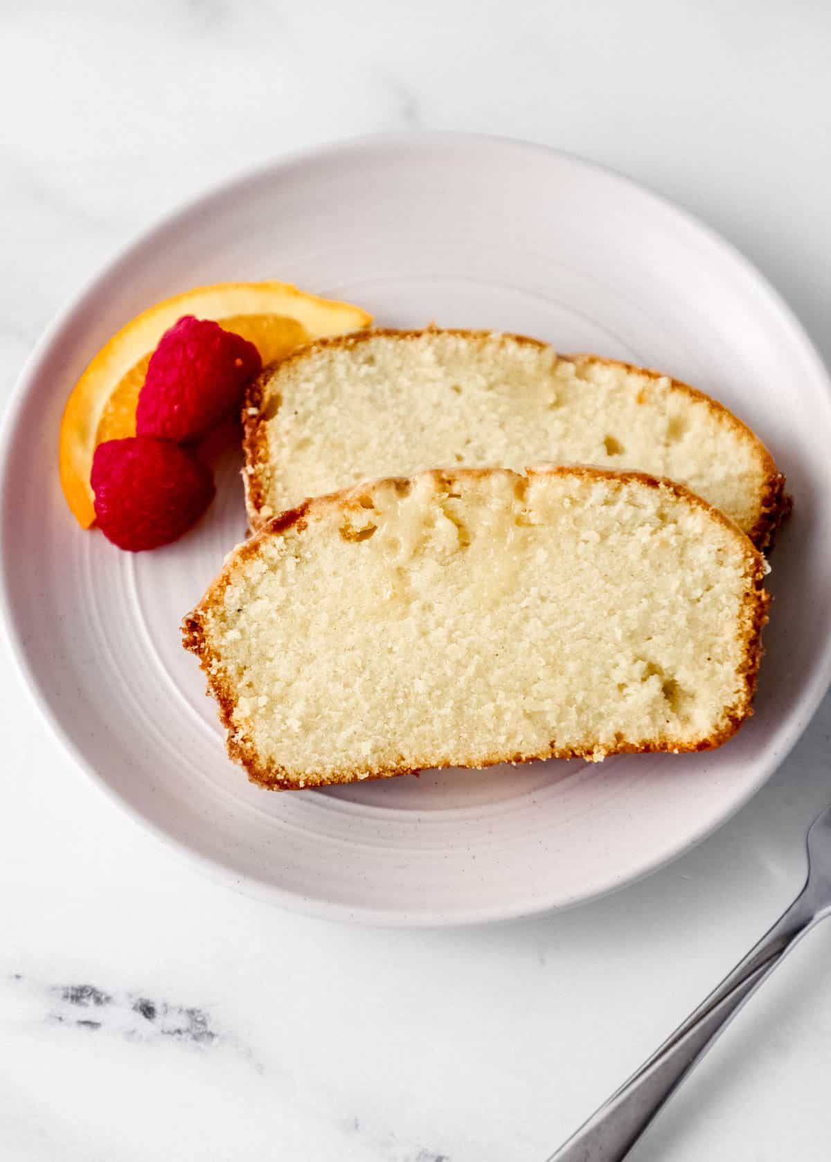 Overhead view of two slices of cake on white plate with fruit beside a fork. 