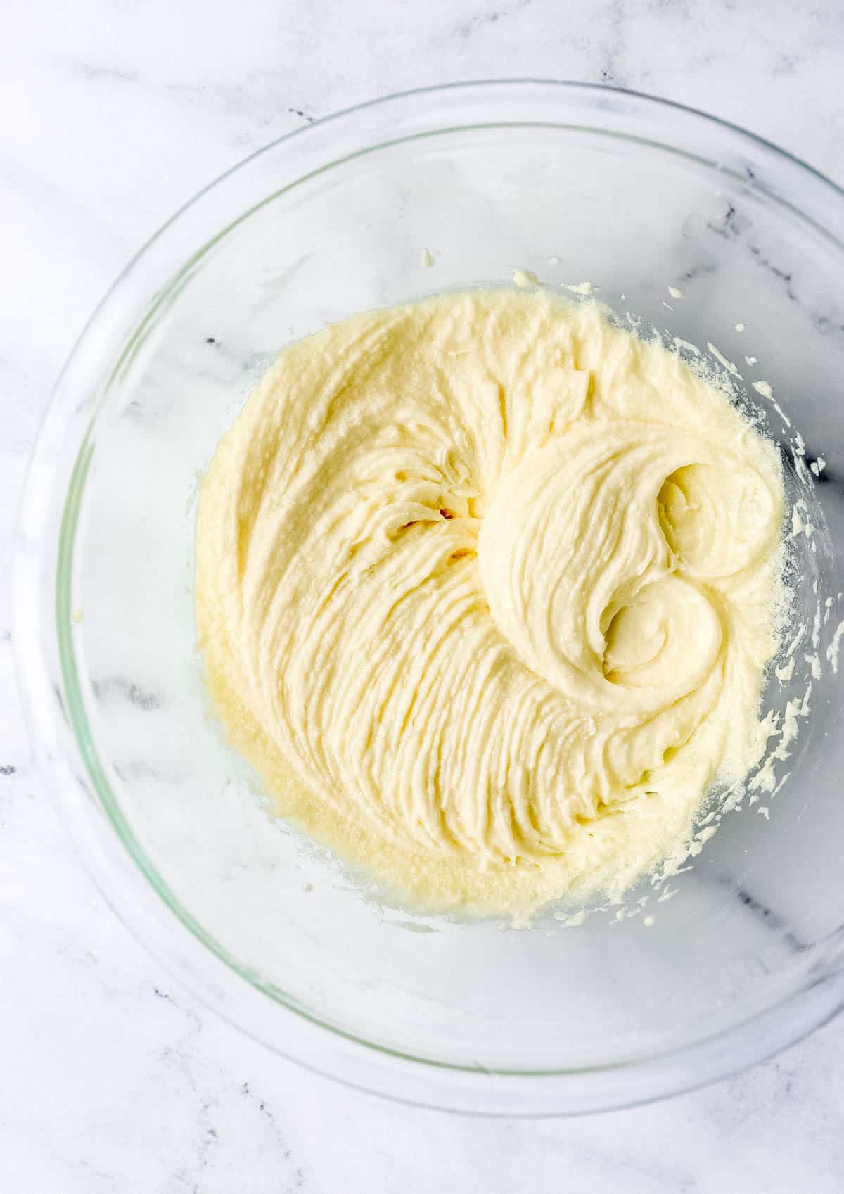 Overhead view of glass mixing bowl with butter, sugar, and eggs, combined. 