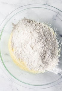 Flour mixture added to cake ingredients in glass mixing bowl.