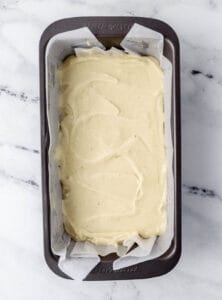 Cake batter added to parchment lined loaf pan.