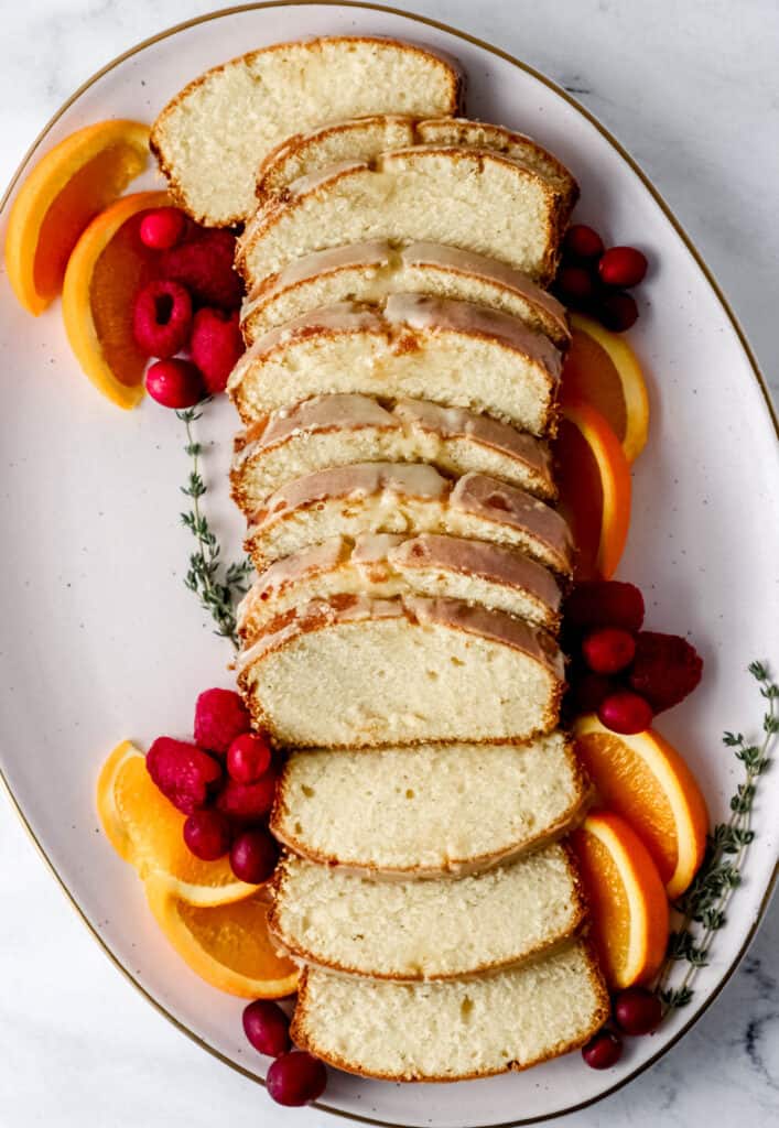 Overhead view of sliced cake on platter with fruit and herbs.