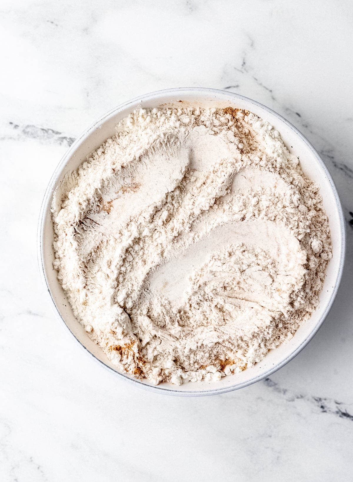 Overhead view of dry cake ingredients combined in white bowl on marble surface.