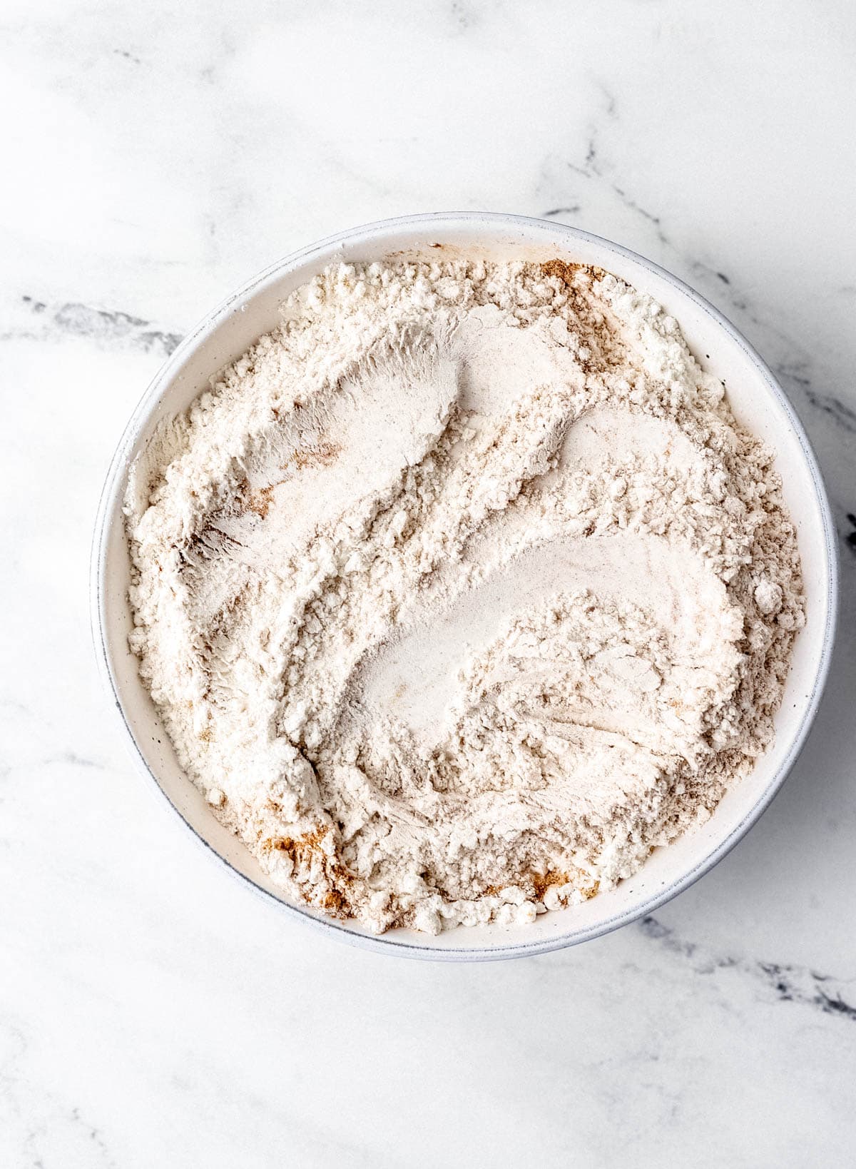 Overhead view of dry cake ingredients combined in white bowl on marble surface. 