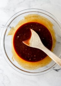 Overhead view of wet ingredients in glass bowl with wooden spoon.