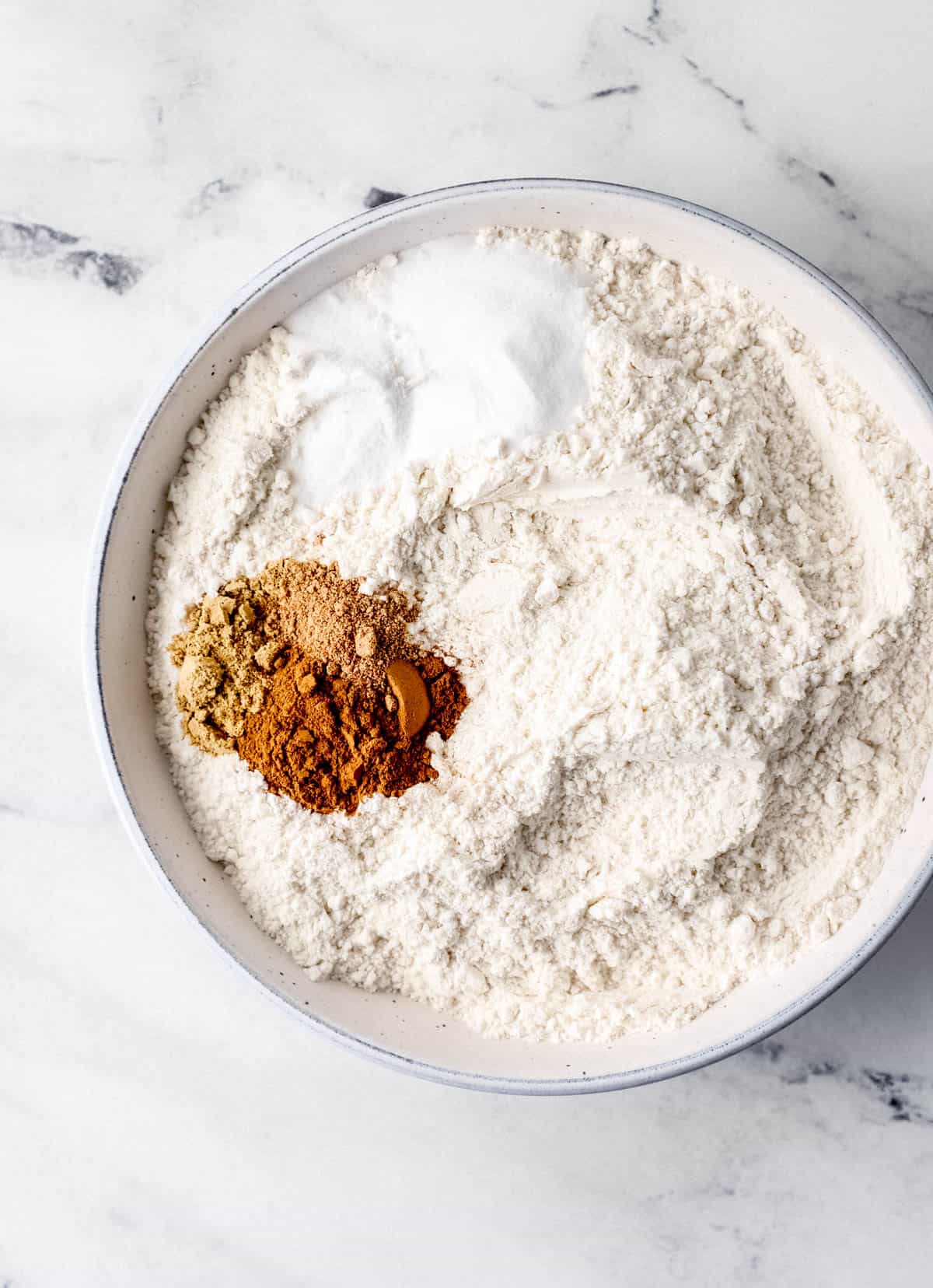 Dry ingredients for muffins in white bowl on marble surface. 