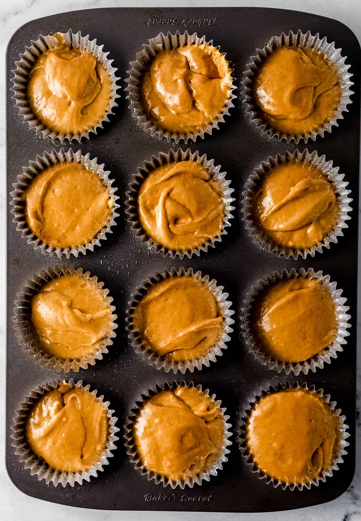 Muffin mixture added to muffin pan with liners before baking. 