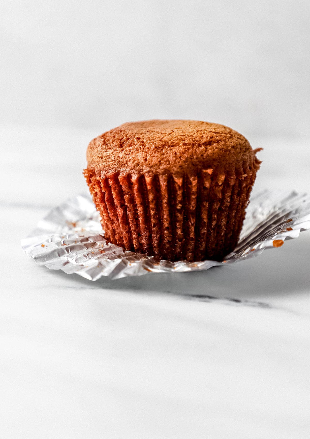 Close up side view of single muffin on top of muffin liner. 