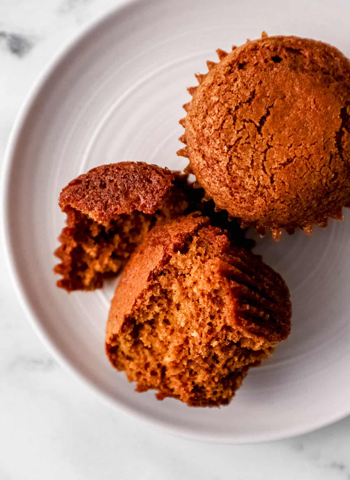 Overhead view of two muffins on white plate, one muffin cut in half. 