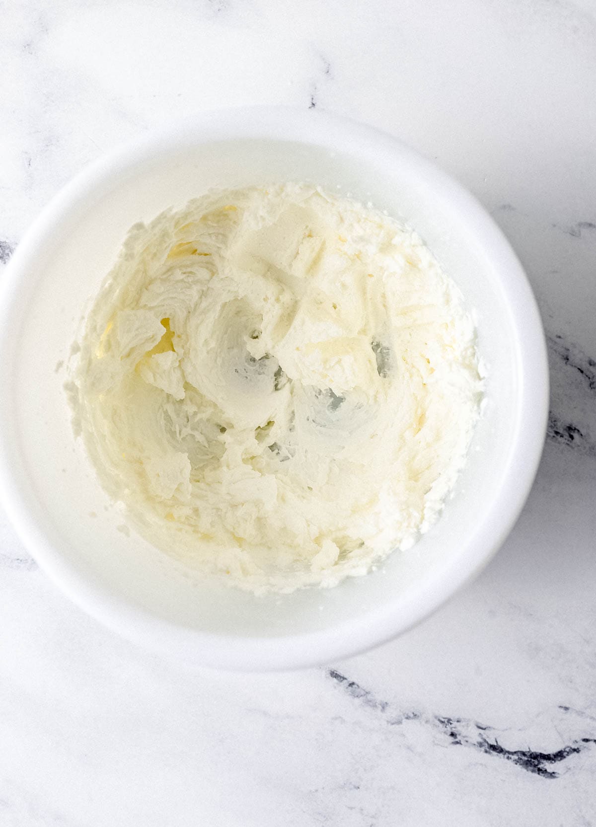 Overhead view of whipped cream in white bowl on marble surface. 