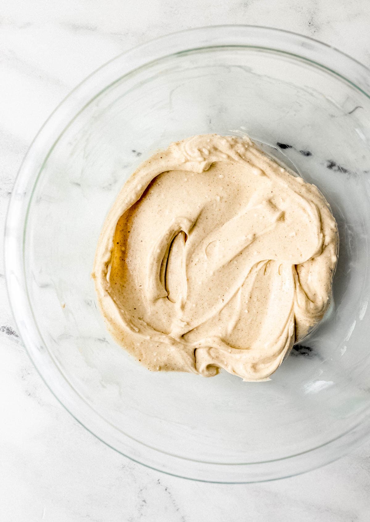 Cheesecake ingredients combined in glass mixing bowl on marble surface. 