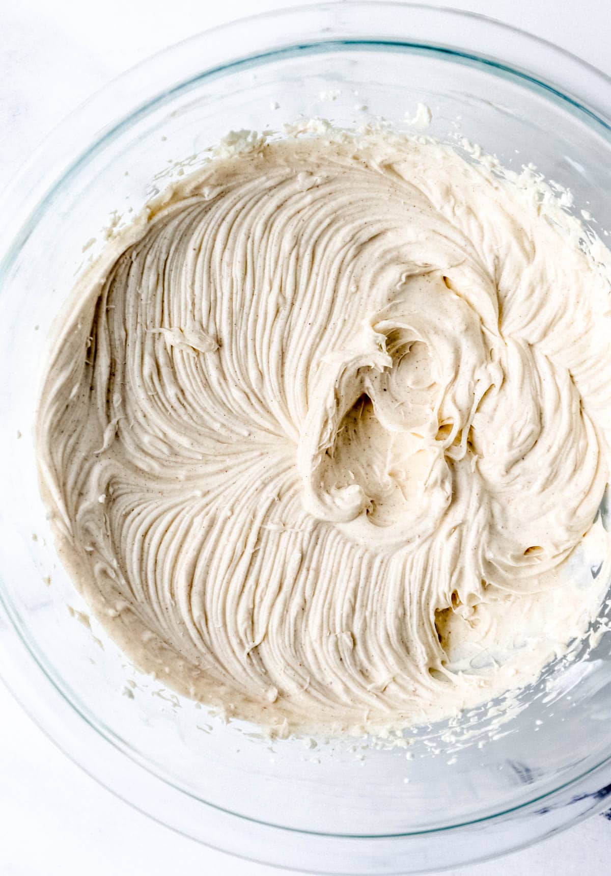 Overhead view of cheesecake filling ingredients combined in glass mixing bowl. 