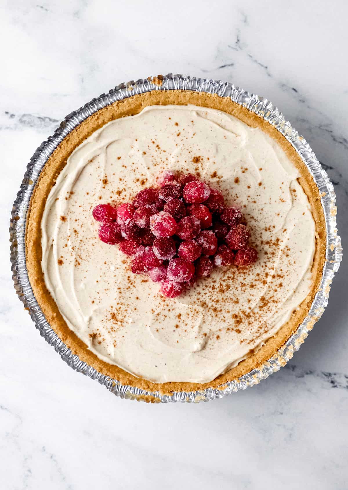 Overhead view of finished eggnog cheesecake topped with sugar cranberries and cinnamon.