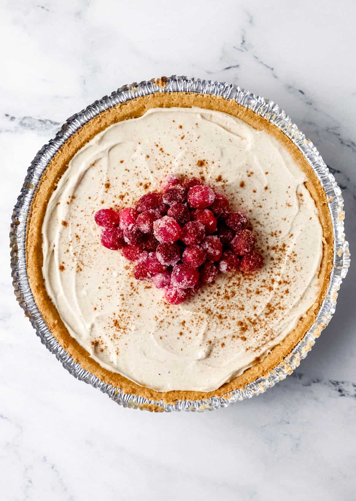 Overhead view of finished eggnog cheesecake topped with sugar cranberries and cinnamon. 