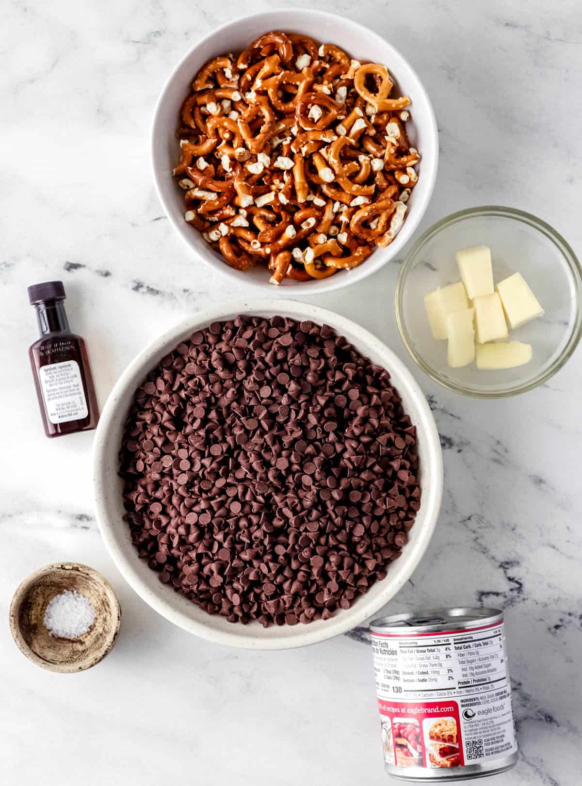 Overhead view of ingredients needed to make fudge in separate bowls and containers on marble surface. 