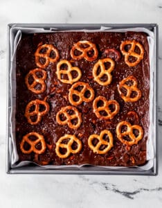Overhead view of fudge topped with pretzels added to parchment lined baking pan.